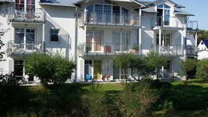 Un edificio residencial de varios pisos con balcones, un porche cubierto y un césped bien cuidado.