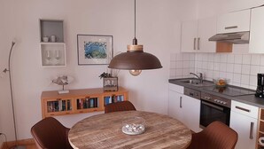 Una cocina compacta con una mesa redonda de madera, dos sillas, una lámpara colgante y un pequeño armario con libros.