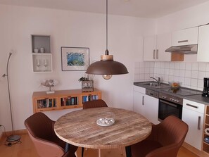 Une cuisine compacte avec une table ronde en bois, deux chaises, une suspension et un petit meuble contenant des livres.