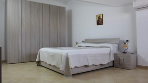 A bedroom with a bed, a nightstand, a lamp, a painting, and an air conditioning unit. - IL GABBIANO (IUN: P5444) (San Giovanni Suergiu)