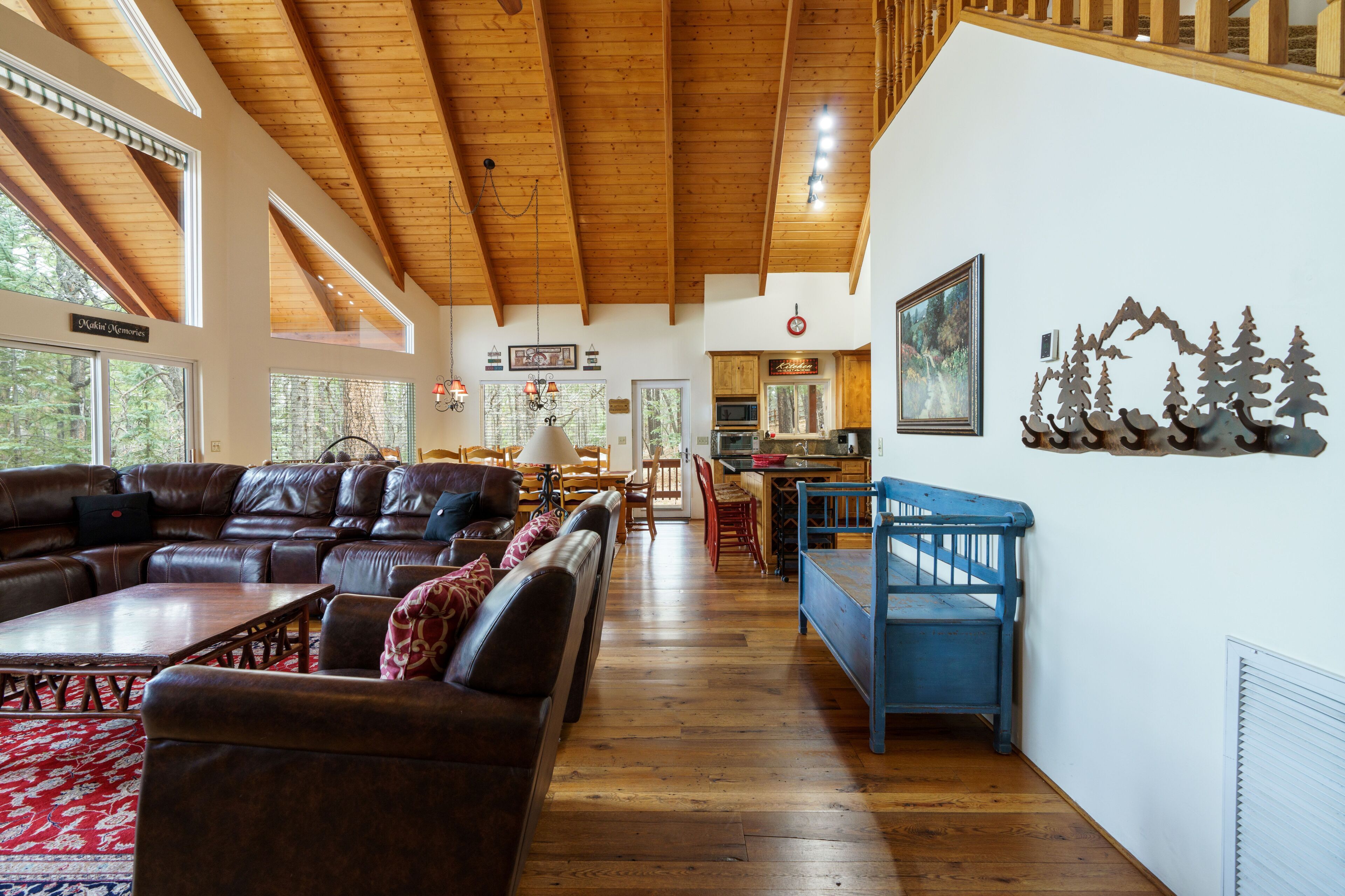 A spacious living room with a large L-shaped sectional sofa, wooden flooring, and a high ceiling with exposed beams.