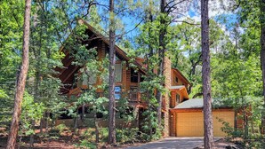A log cabin with a garage and a covered porch, surrounded by trees.