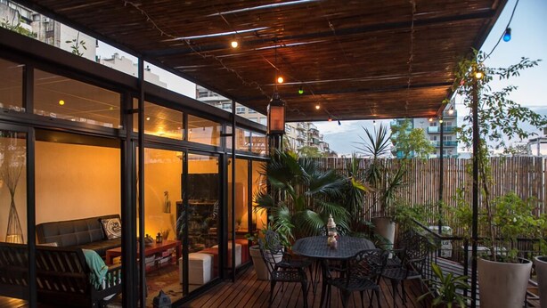 An outdoor patio with a wooden deck, round tables, and chairs, surrounded by potted plants and a bamboo fence. - La Casa de Bulnes (Buenos Aires)