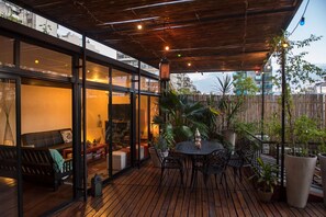 An outdoor patio with a wooden deck, round tables, and chairs, surrounded by potted plants and a bamboo fence. - La Casa de Bulnes (Buenos Aires)