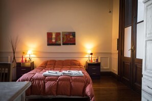 A neatly made bed with a red blanket, two bedside tables with lamps, and two abstract paintings on the wall.
