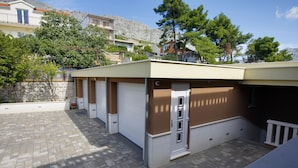 Un bâtiment doté d’un espace de stationnement couvert, d’un escalier et offrant une vue sur les maisons et les arbres environnants.