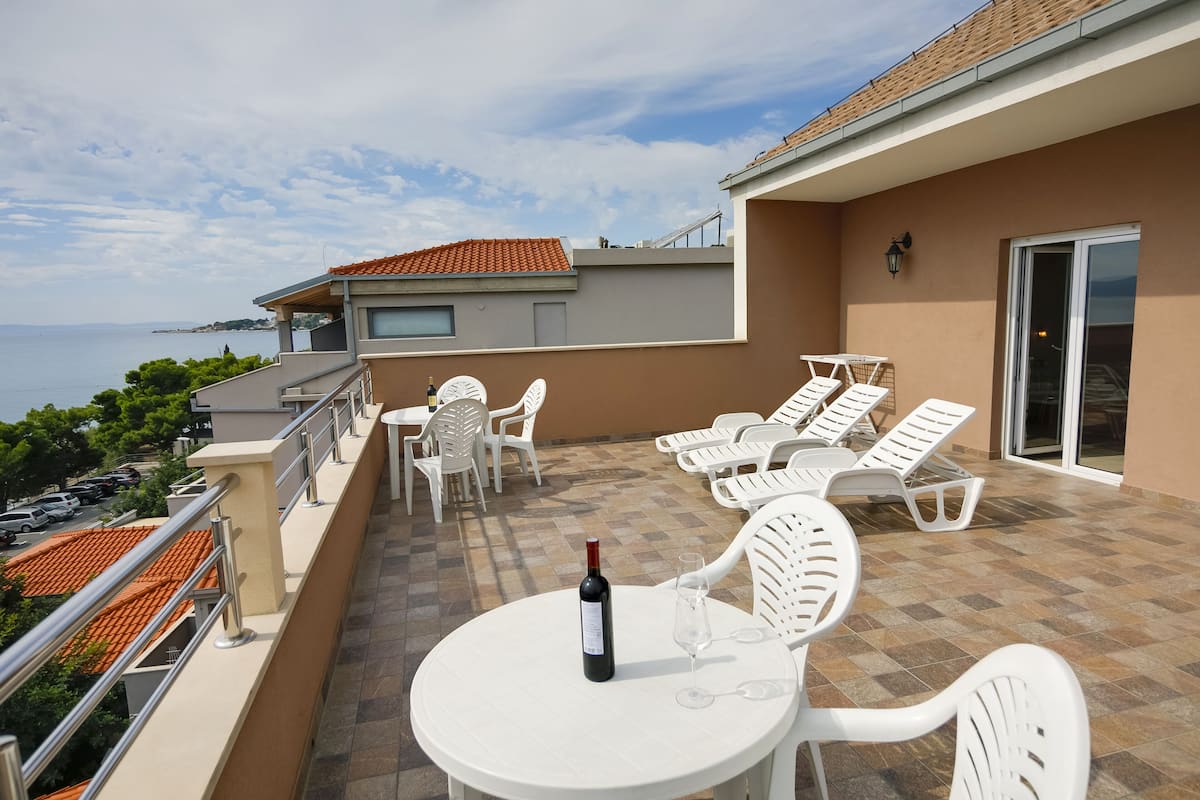 A balcony with white chairs and a table, a bottle of wine, and a glass on the table.