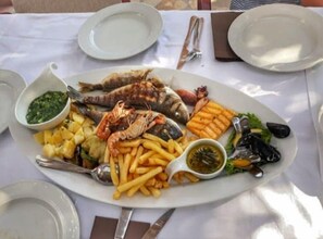 A seafood platter with various fish, prawns, fries, and sauces on a table. - Pansion Dalmacija (Dugi Rat)