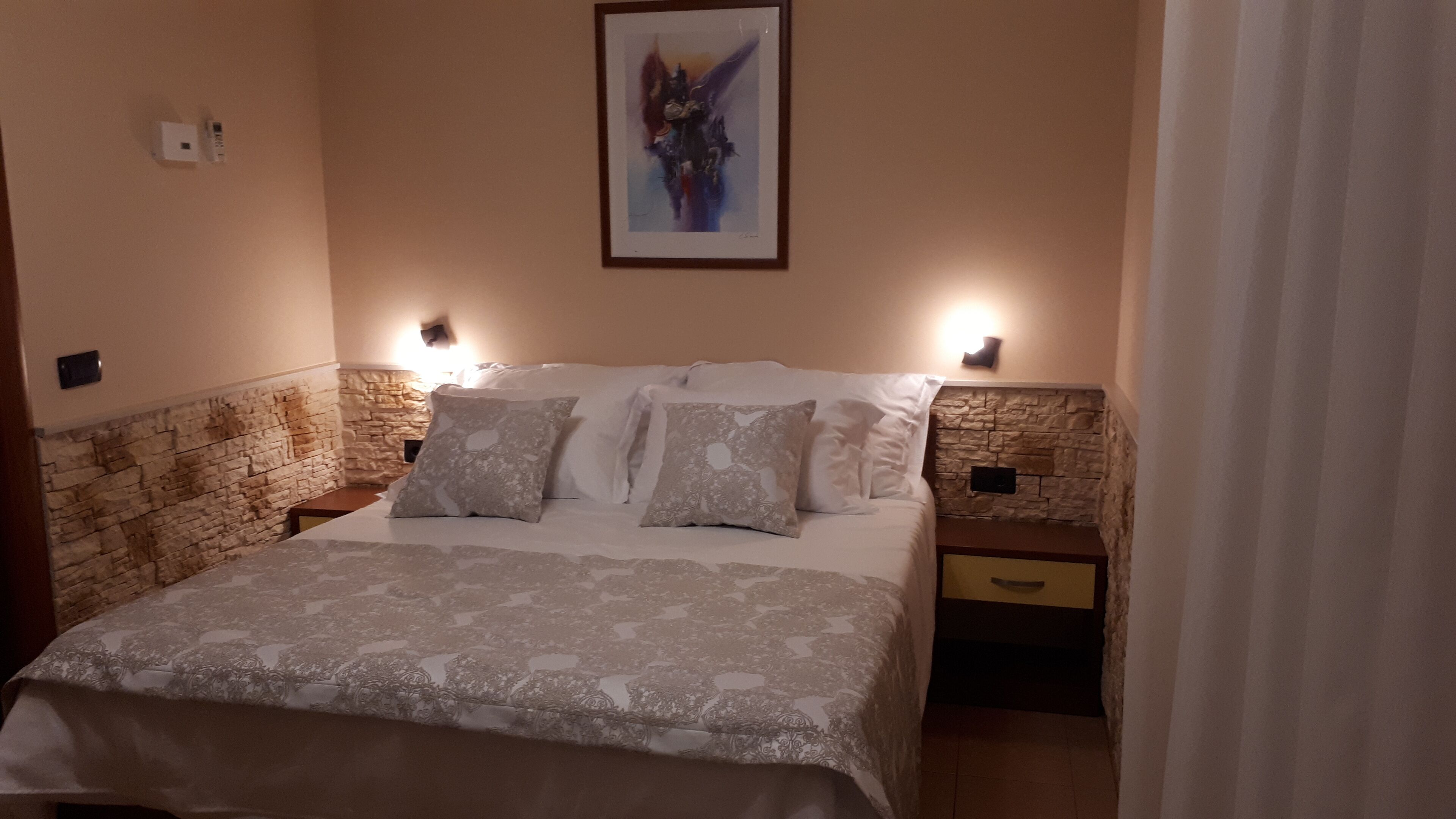 A bedroom with a stone wall, a bed with patterned bedding, two bedside tables, and a framed artwork on the wall.