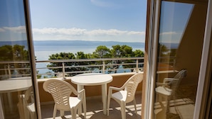Un balcon avec une table et des chaises, donnant sur une étendue d’eau et un espace verdoyant.