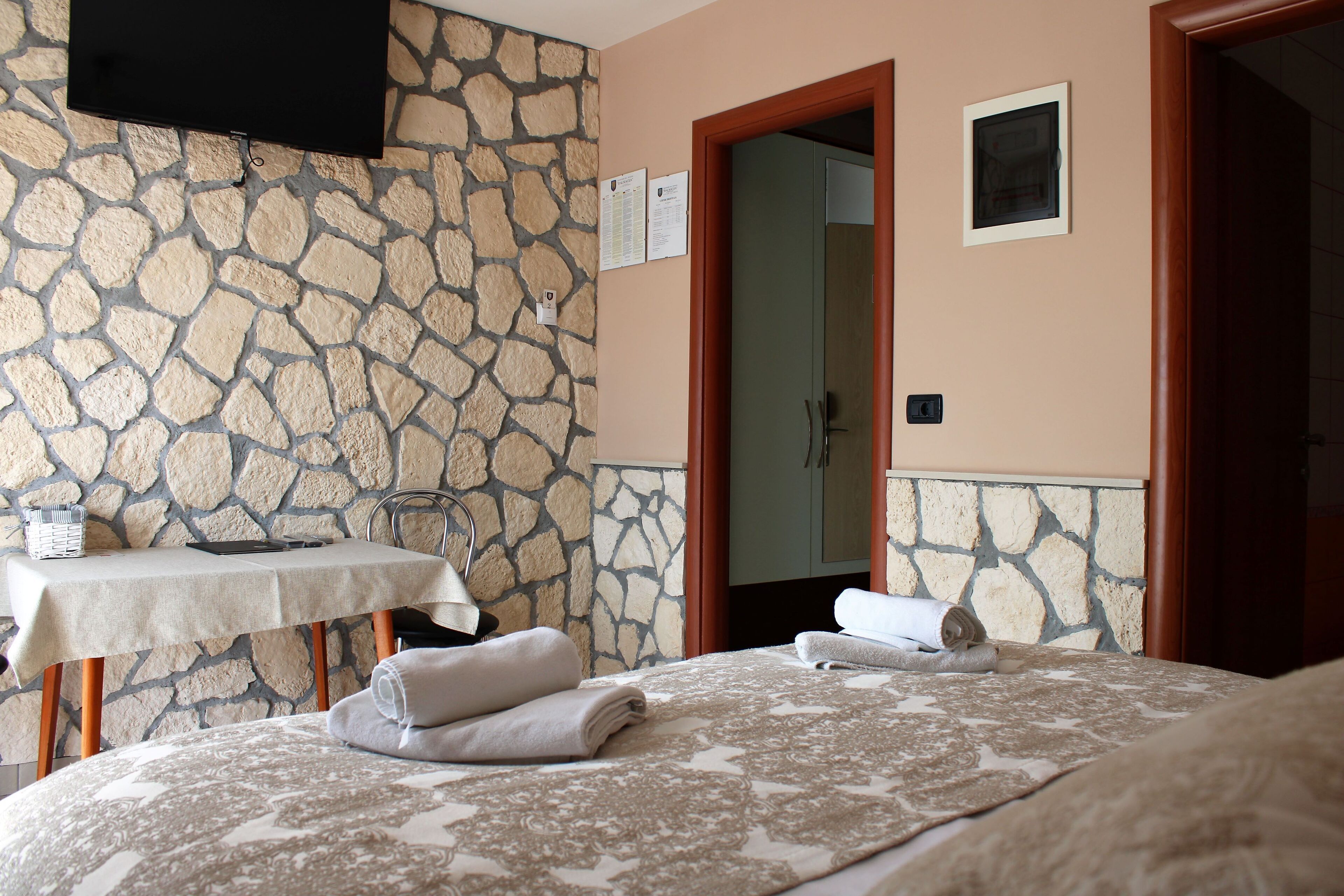 Une chambre d’hôtel avec un mur en pierre, un lit recouvert d’une couvre-lit à motifs, une table avec une lampe et un téléviseur fixé au mur.