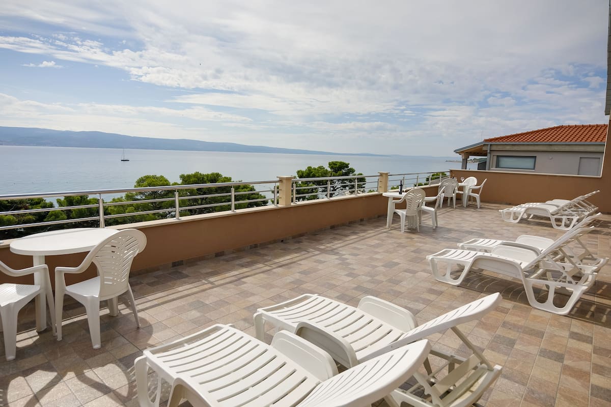 A terrace with white plastic chairs and tables, overlooking a body of water and distant mountains.