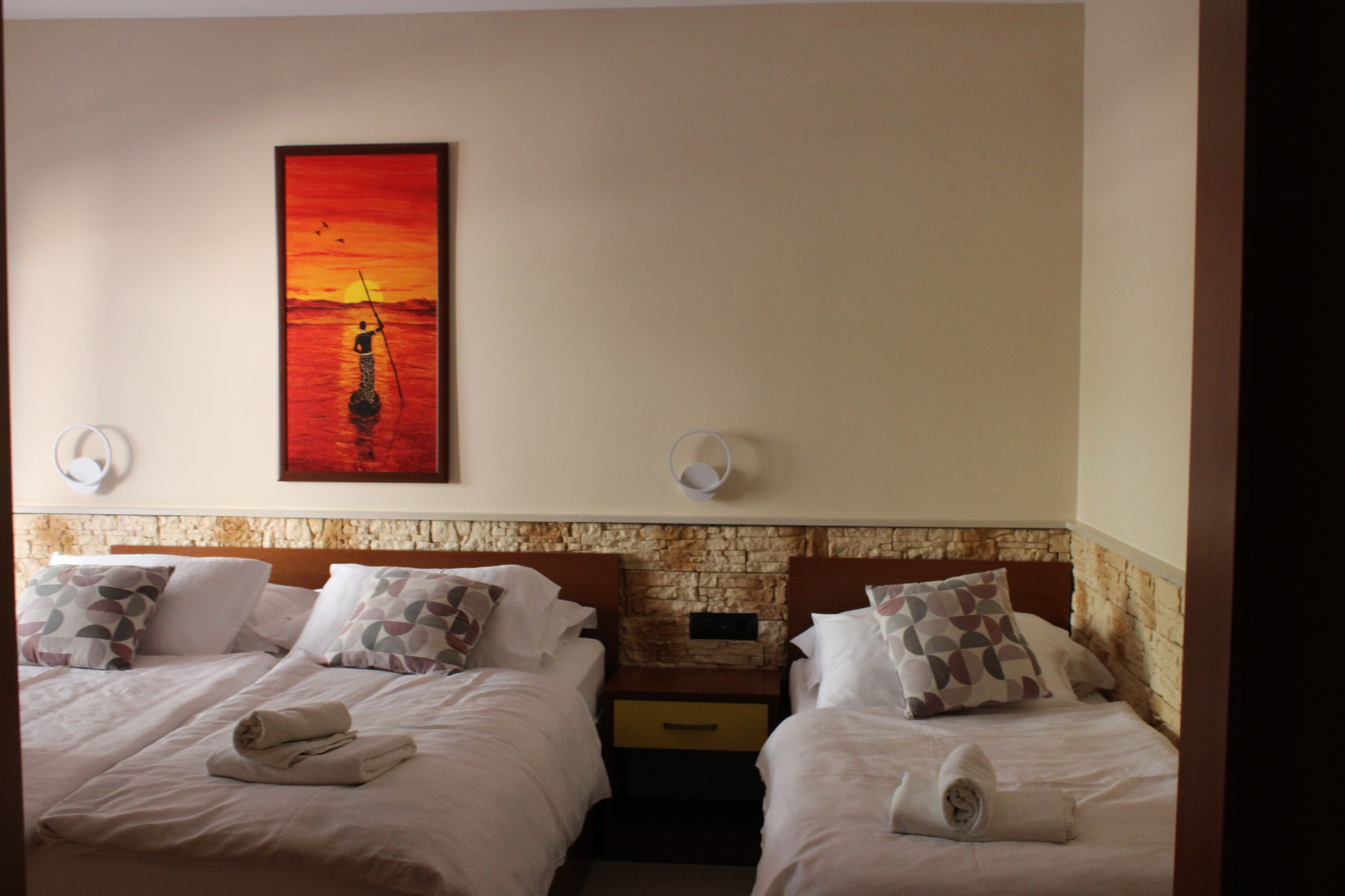 Camera d'albergo con due letti, un muro in pietra e un dipinto del tramonto.