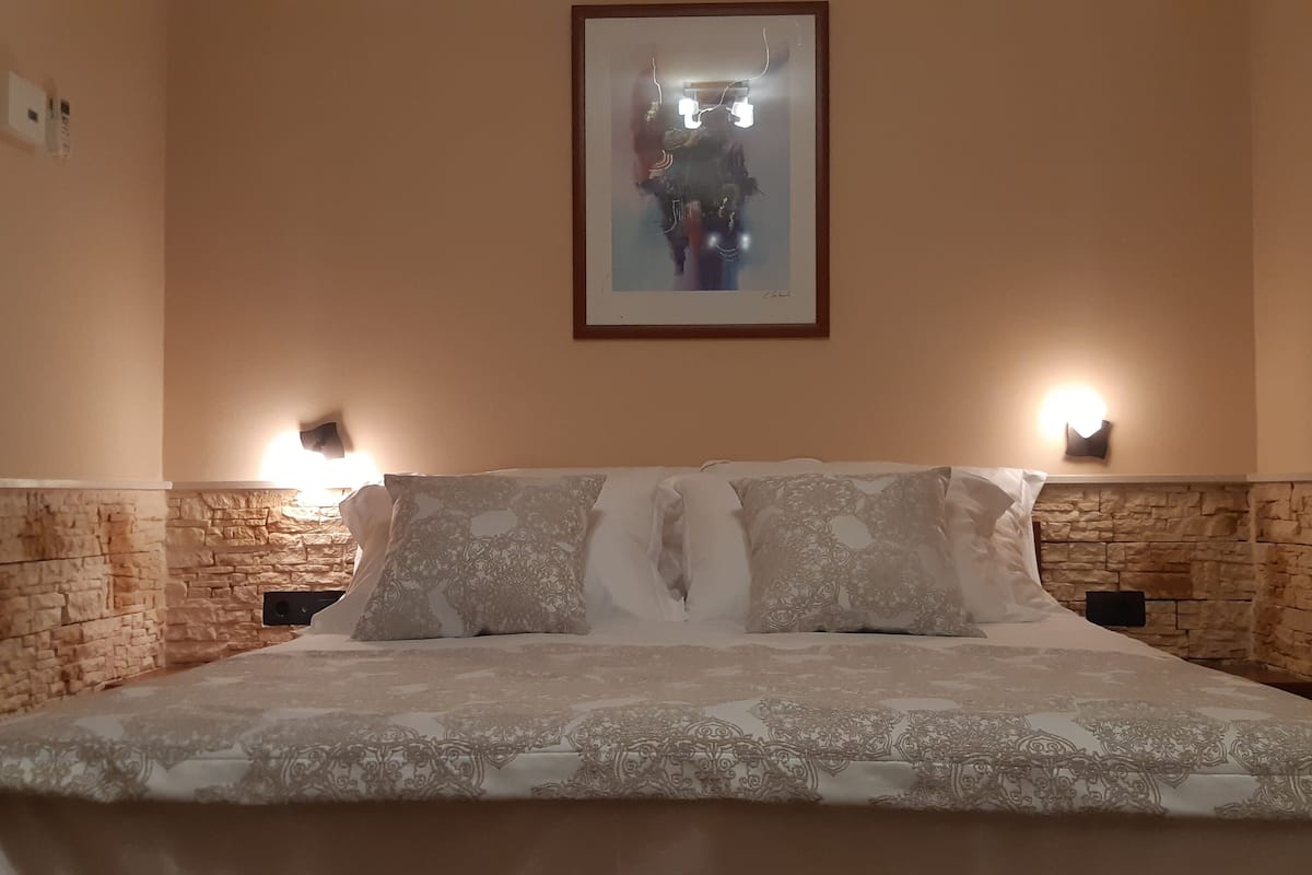 A bed with patterned bedding, two wall-mounted lights, and a framed picture above the bed.