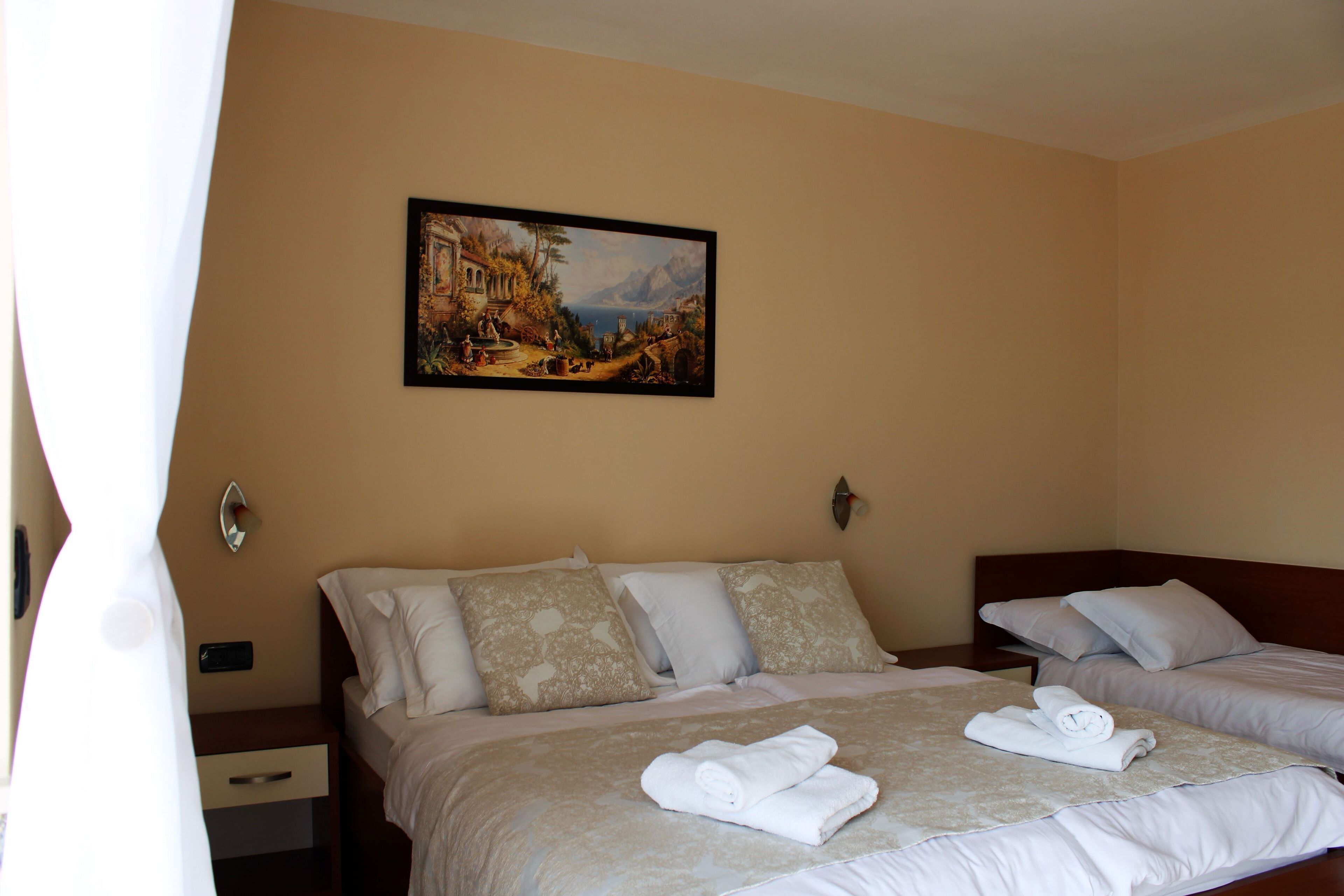A hotel room with two beds, a painting on the wall, and a nightstand with a lamp.