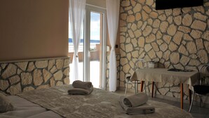 Une chambre d’hôtel avec un lit, une table et une chaise. Il y a un mur en pierre et une vue sur la mer.