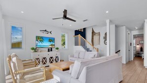 A spacious living room with a white sofa, a wooden coffee table, and a TV displaying a tropical beach scene. - Luxury Beach Retreat:  Rooftop Views, Pool and Spa (Bradenton Beach)