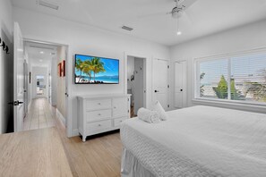 Een moderne slaapkamer met een groot bed, een flatscreen-tv en uitzicht op palmbomen door het raam.