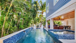 A swimming pool with blue mosaic tiles, surrounded by lush tropical plants and a covered outdoor seating area. - Luxury Beach Retreat:  Rooftop Views, Pool and Spa (Bradenton Beach)