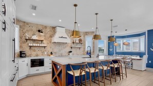 A modern kitchen with a central island, bar stools, pendant lighting, and nautical-themed decor. - Luxury Beach Retreat:  Rooftop Views, Pool and Spa (Bradenton Beach)