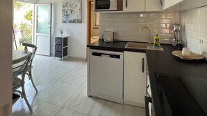 A modern kitchen with white cabinets, a black countertop, and a dishwasher. There is a dining area with a table and chairs visible through an open door. - Apartments Matea with Infinity Pool (Cesarica)