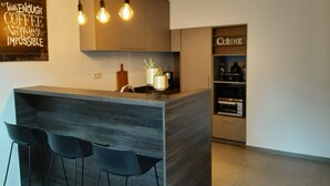 Une cuisine moderne dotée d’un bar, de luminaires suspendus et d’un panneau sur lequel on peut lire : « Avec suffisamment de café, rien n’est impossible. »
