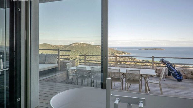 Un balcone con vista sul mare, pavimento in legno e zona salotto esterna.