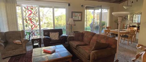 A cozy living room with a fireplace, a dining area, and a large window with a view of greenery.