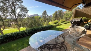 Eine Terrasse mit Glastisch und Korbstühlen, mit Blick auf einen gepflegten Rasen und ferne Berge.