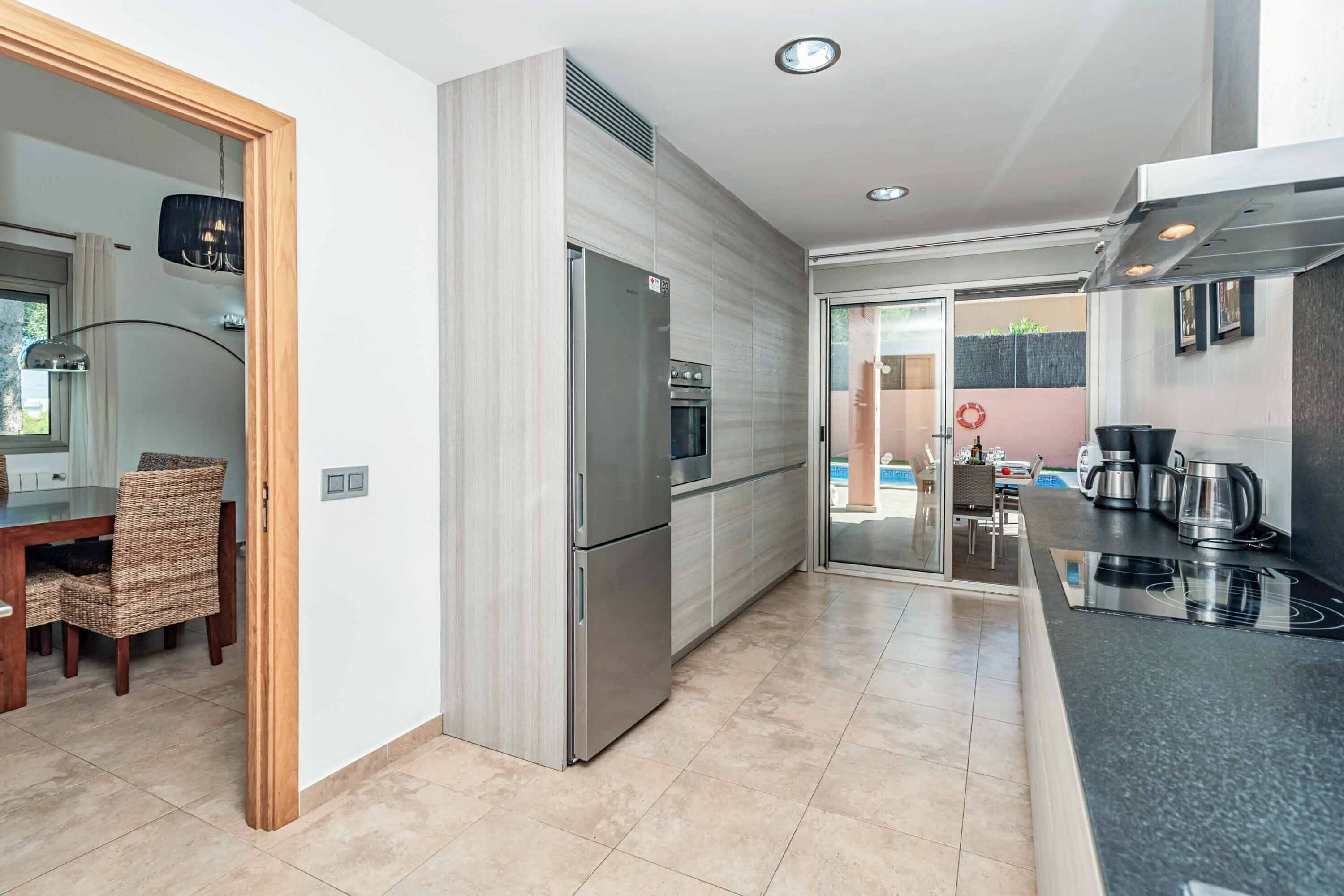 A modern kitchen with stainless steel appliances, a dining area with wicker chairs, and a view of the outdoors through a glass door.
