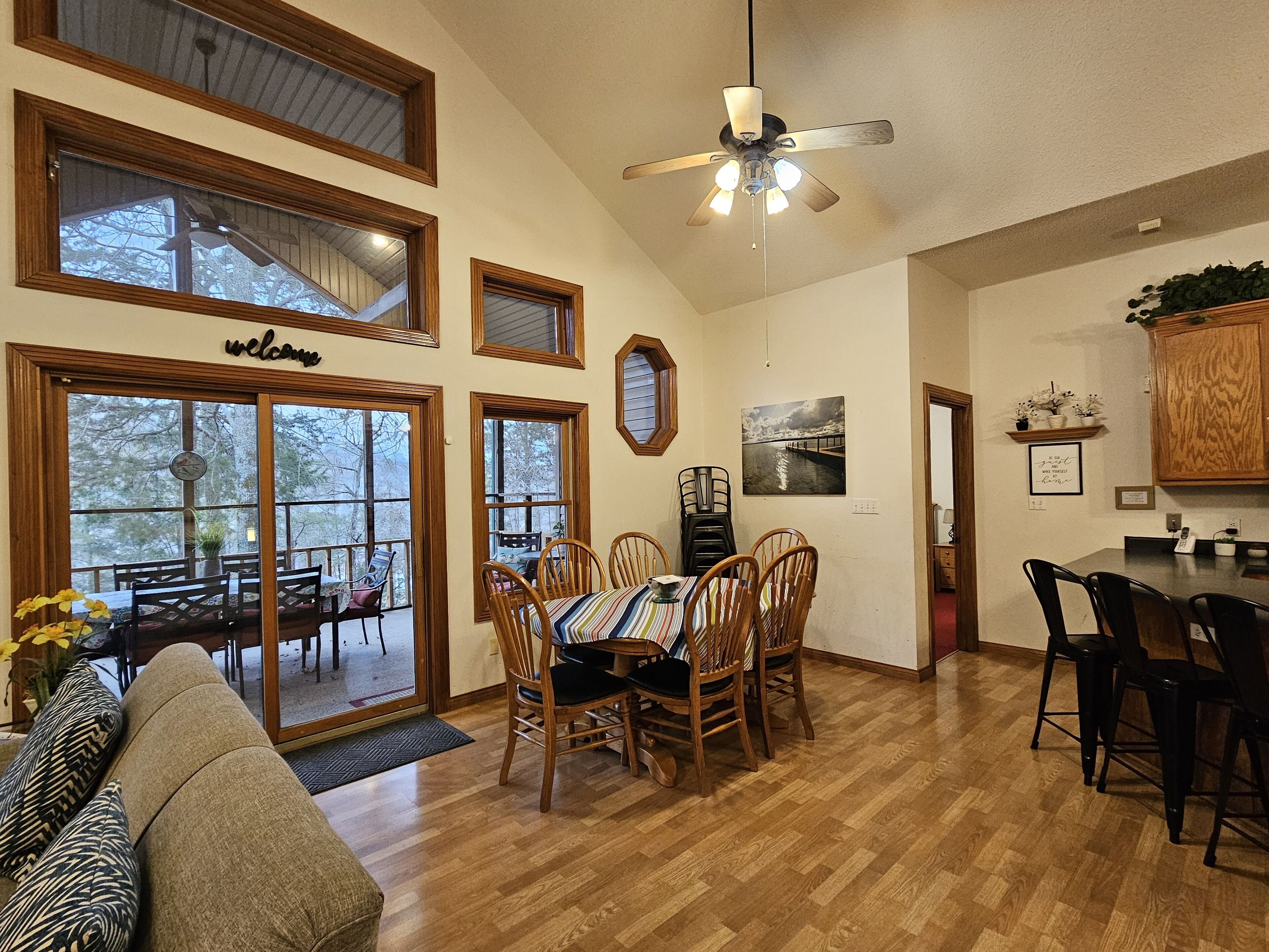 A spacious dining area with wooden chairs and a table, large windows, and a ceiling fan.