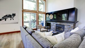 A modern living room with a stone fireplace, a large window, and a gray sectional sofa.