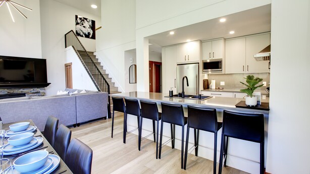 A modern kitchen with a central island, bar stools, and a dining area with blue plates and glasses.