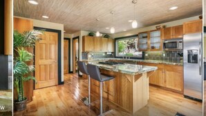 Una cucina moderna con mobili in legno, un'isola centrale con sgabelli da bar, elettrodomestici in acciaio inossidabile e una pianta in vaso.
