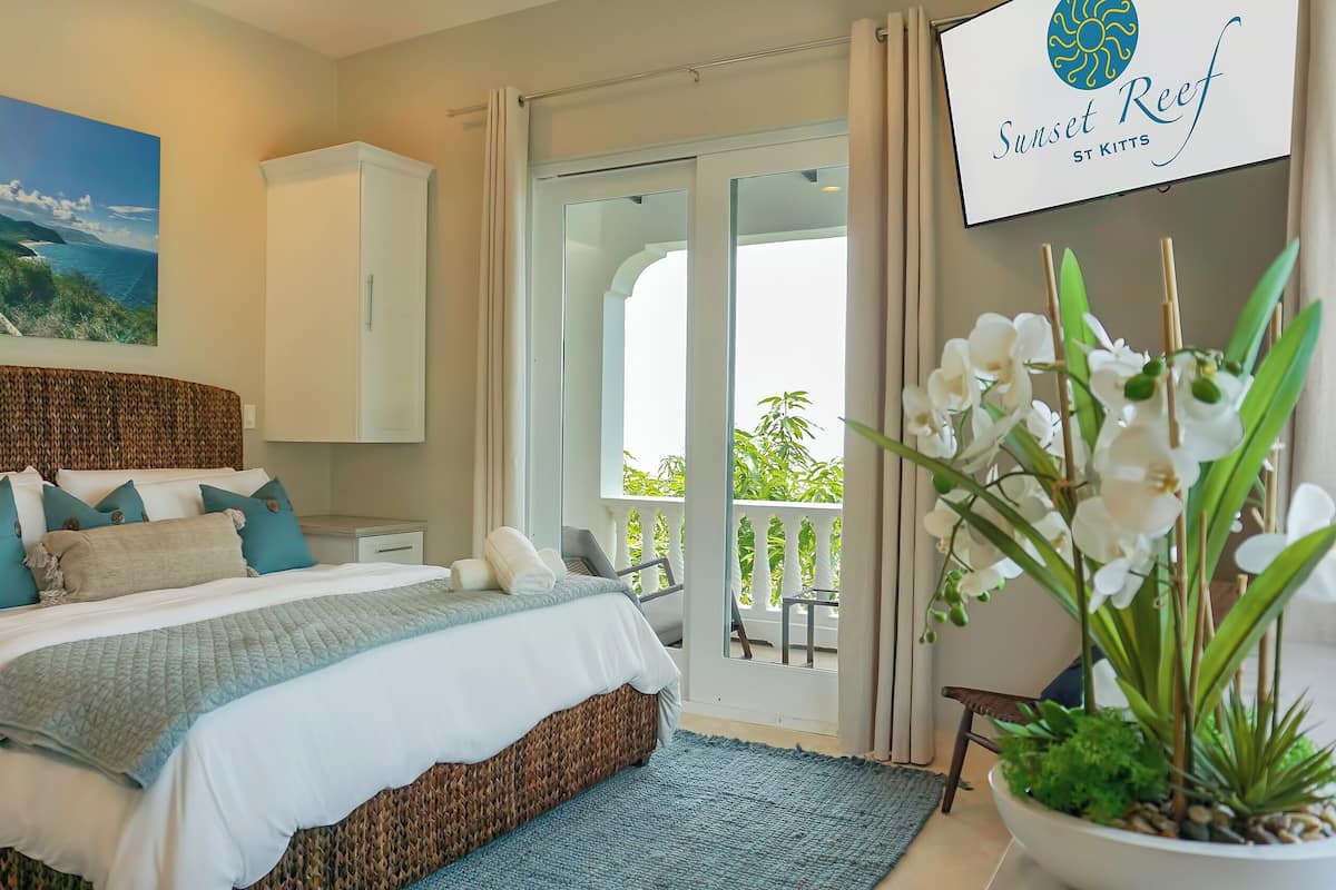 A bedroom with a bed, a nightstand, a potted plant, and a view of the outdoors.