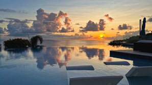 Una piscina infinita tranquila con vista al atardecer, una estatua y un pequeño jardín.