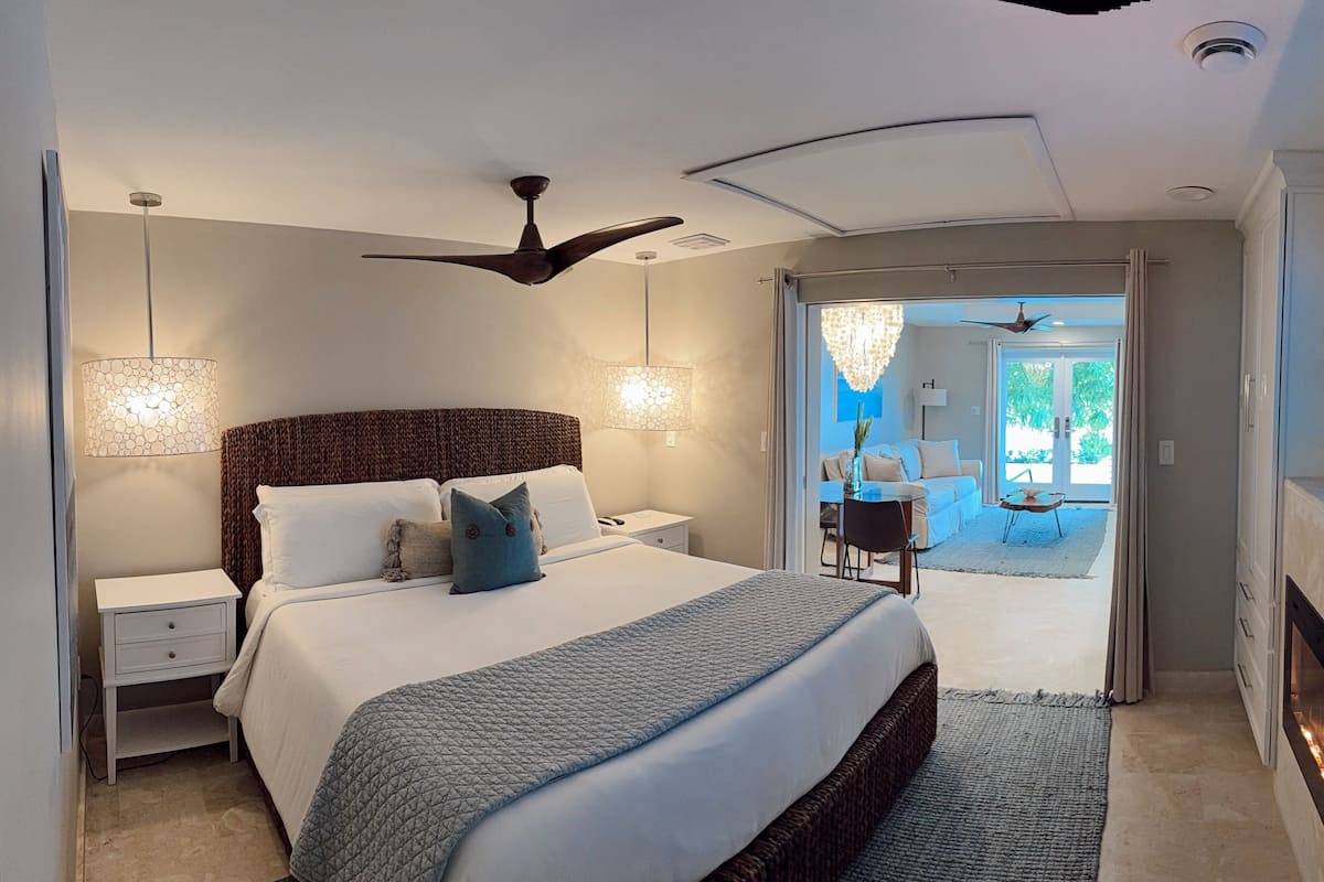 A modern bedroom with a large bed, bedside lamps, a ceiling fan, and a fireplace.