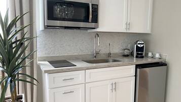 A modern kitchen with white cabinets, a stainless steel microwave, a dishwasher, and a coffee maker.