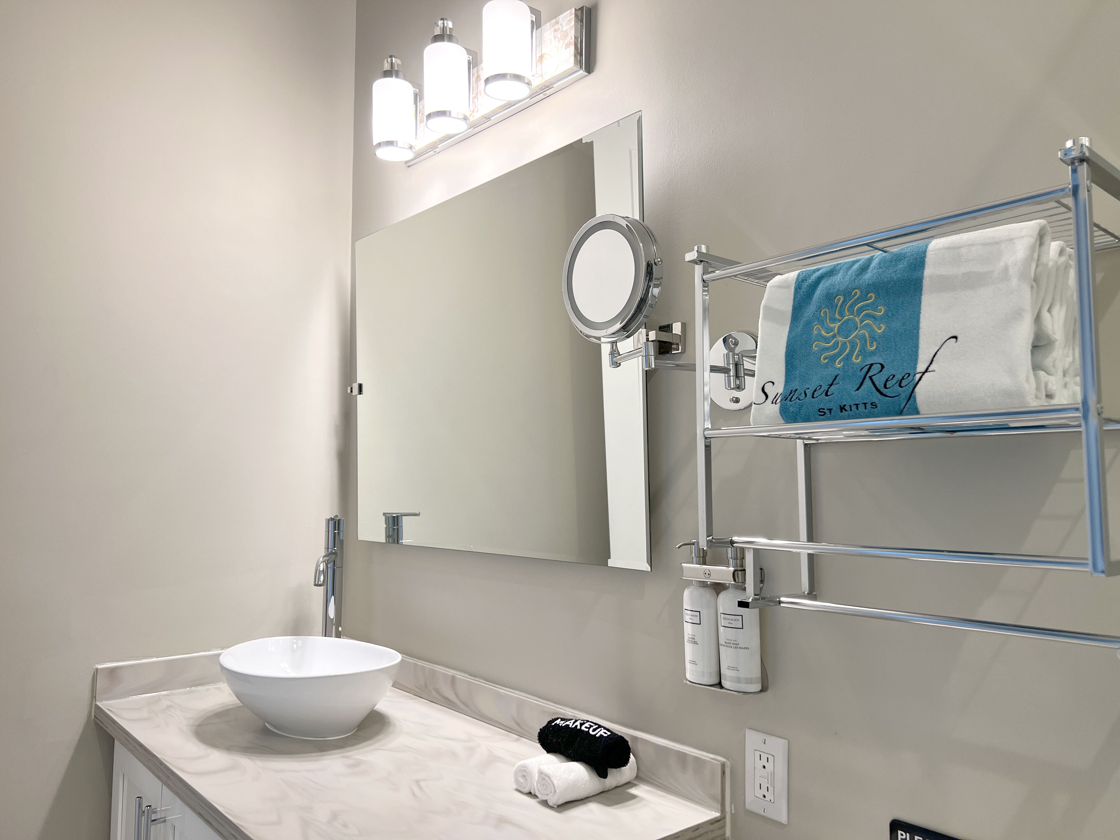 Un baño moderno con un lavabo blanco, un espejo grande y un toallero con una toalla.
