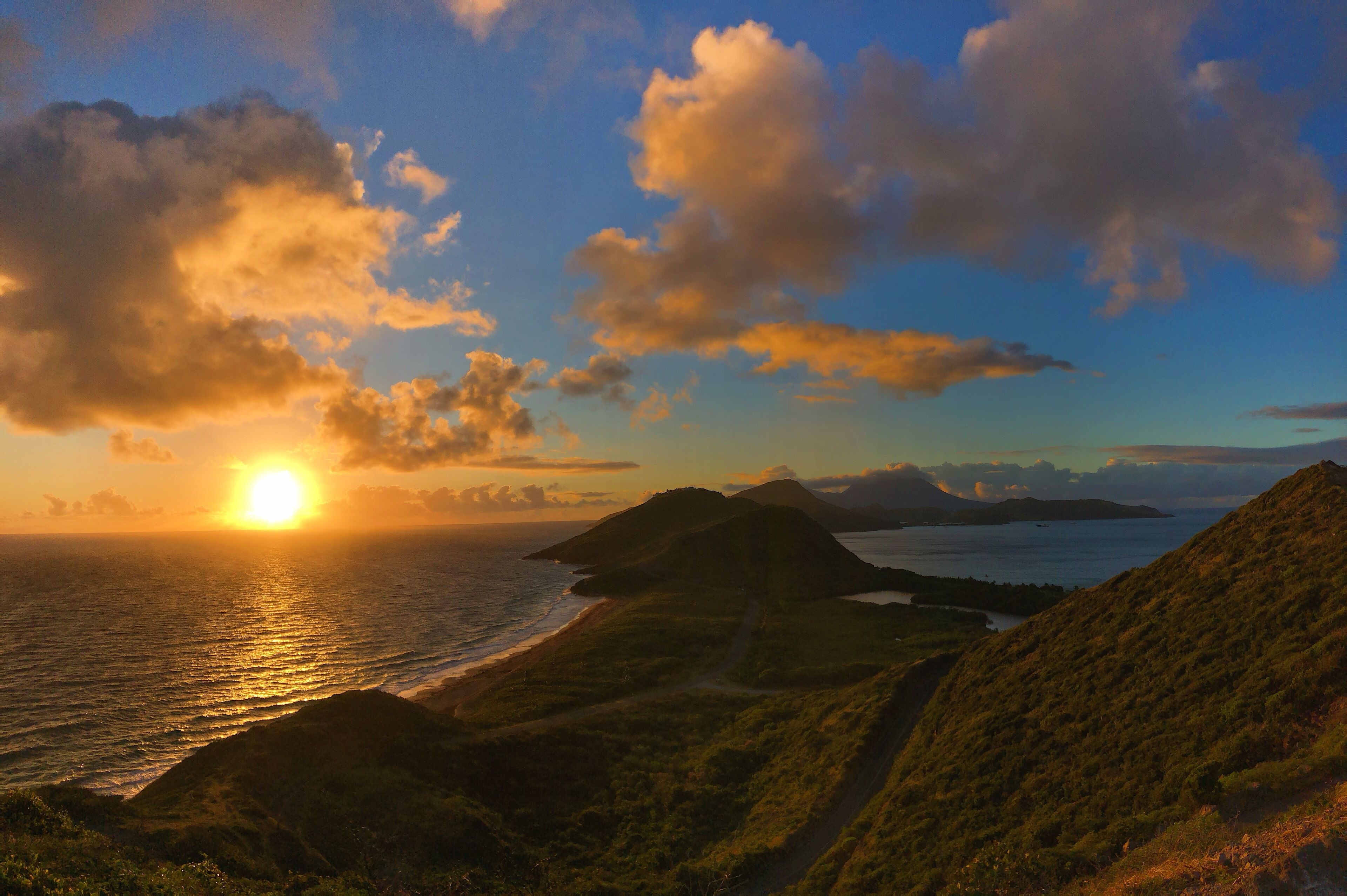 A coastal landscape with a sunset, hills, and a path leading to the water.