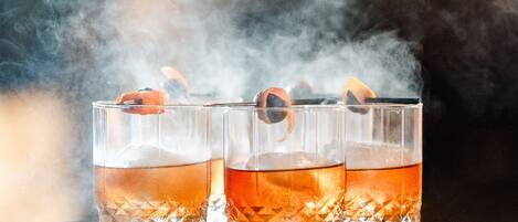 Three glasses of amber liquid on a tray with ice cubes, held by a hand.