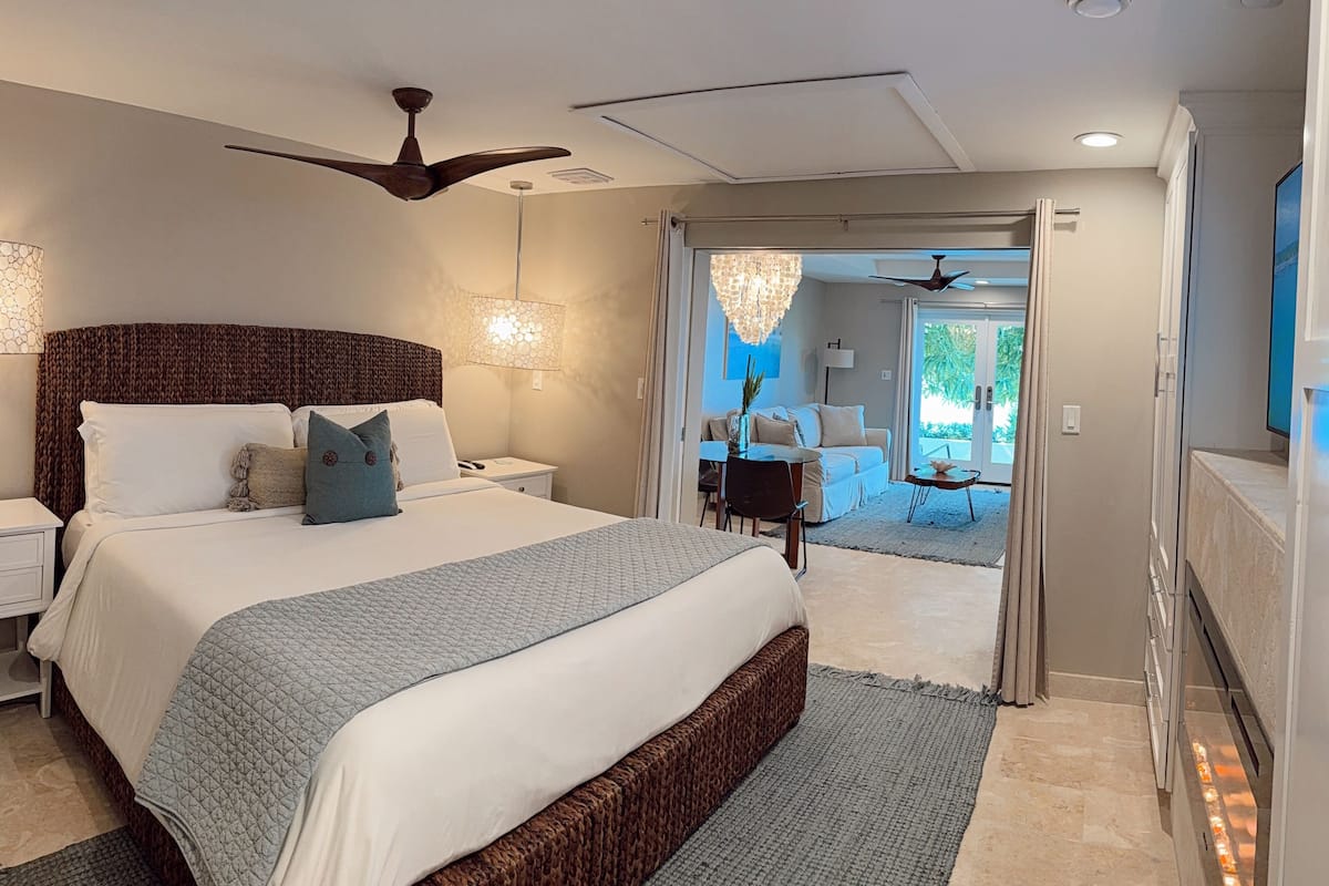 A modern bedroom with a large bed, a ceiling fan, and a view to a balcony.