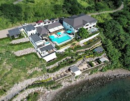 An aerial view of a property with a swimming pool, multiple buildings, and a rocky shoreline.