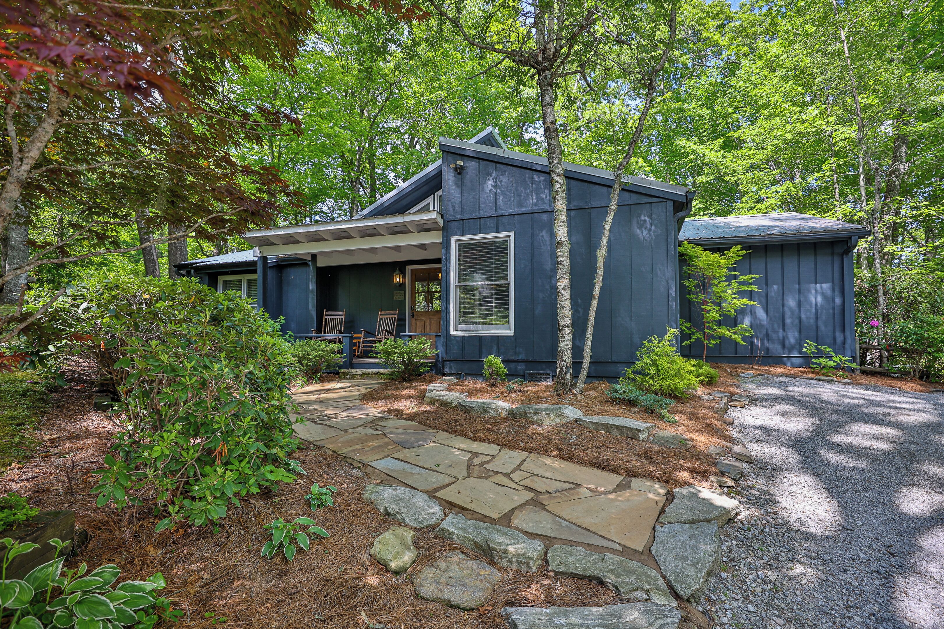 A modern house with a stone pathway leading to the entrance, surrounded by lush greenery.