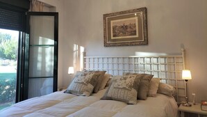 A bedroom with a large bed, a chandelier, a framed picture on the wall, and a window with curtains.
