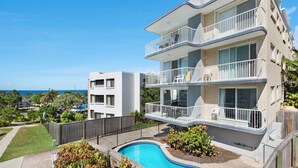 A multi-story residential building with balconies, a swimming pool, and a view of the ocean.