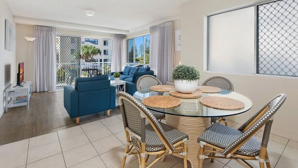 A modern living room with a glass dining table, wicker chairs, a sofa, and a balcony with curtains. - Spinnaker Seas Steps To Kings Beach | Ocean Views | Pool (Kings Beach)