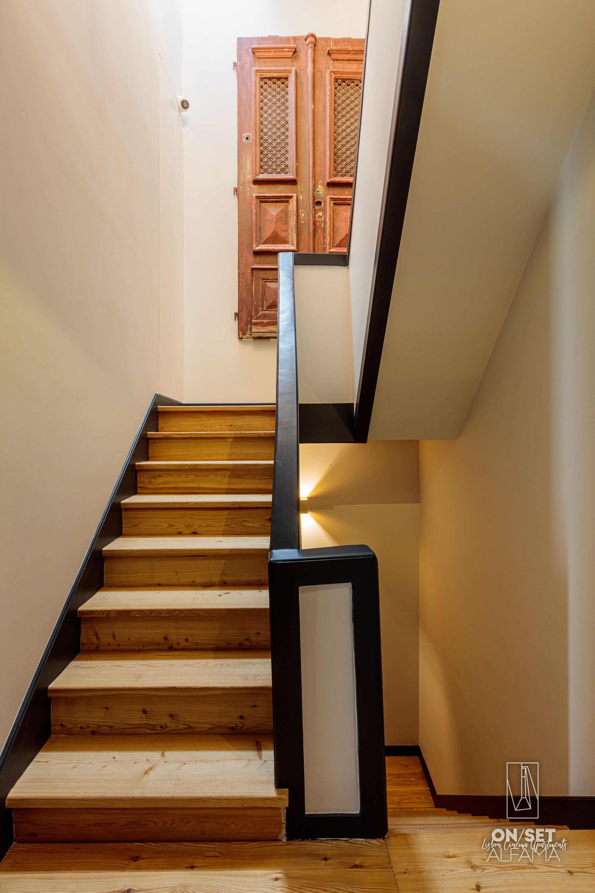 Eine Holztreppe mit schwarzer Handläufe führt zu einer Tür mit einem Holzpaneel-Design.