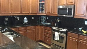 A kitchen with wooden cabinets, a stainless steel microwave, a stove, and a granite countertop. - Ocean Front, Luxurious 3/3 New Rental (Daytona Beach Shores)