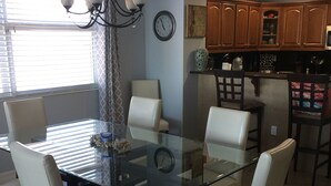 A dining area with a glass table surrounded by four chairs, a chandelier, and a clock on the wall. - Ocean Front, Luxurious 3/3 New Rental (Daytona Beach Shores)